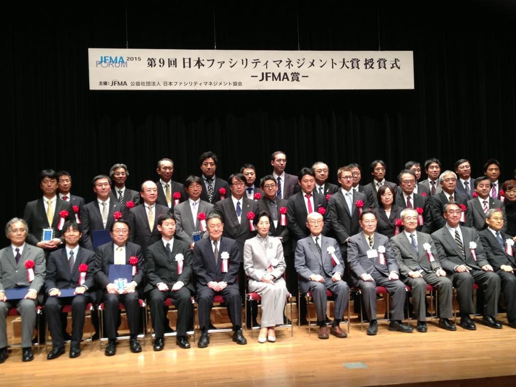 「JFMA2015 第9回日本ファシリティマネジメント大賞 授賞式」の看板の下での受賞者と主催者の集合写真
