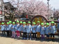 桜の木が咲く保育園前での園児たちの集合写真