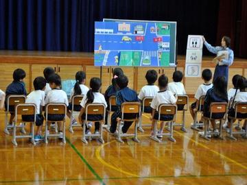 小学校の体育館で児童が婦警さんに教わっている交通安全教室の写真