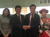 理事長と市長が握手している右ににたすきをつけた赤い服の方左にもうひとりと4人で並んでいる写真