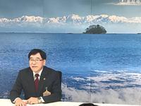 島が見える海の写真の前に着席し記者会見をする市長の写真