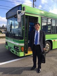 ドアの開いた緑色のバスの前に立つ市長の写真