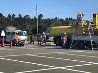 駐車場で関係者3人が近くにいる黄色のタンク車に放水している方たちの写真