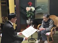 椅子に座る高齢の女性に賞状を手渡す市長の写真