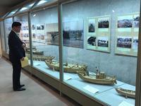 ドブネ復元特別展：ケース越しに木造船の模型を眺める市長の写真