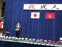 国旗と市旗が飾られている幕の前で市長が話をしている写真
