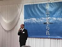 元気とやま創造懇談会の会場で「富山に来られ。」の文字が書かれている垂れ幕を前にスピーチをする市長の写真
