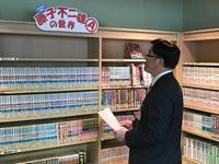 漫画がぎっしり展示された本棚を見ている市長の写真