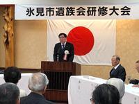 遺族会研修大会で日本の旗の前の演壇に立つ市長の写真
