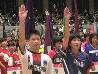 体育館内で代表選手の2人が右手をあげ選手宣誓している写真