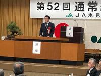 総代会で日本の旗とJAの旗の前の演壇に立つ市長の写真