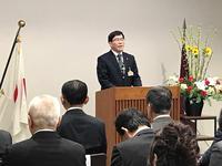 表彰式で日本の旗が右にたてられた演壇に立つ市長の写真