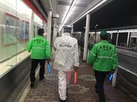 夜間にパトロールをする白い服装の人と緑のジャケットを着た2名の人が歩いている後ろ姿の写真