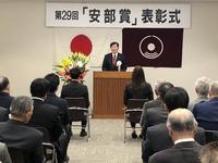 表彰式で日本の旗と氷見市章の旗が貼られた壁面前の演壇に立つ市長の写真