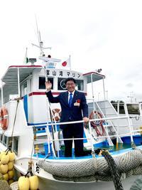 クルージング船の最前部甲板に立って手をあげている市長の写真