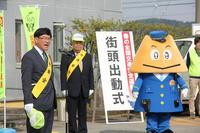街頭出動式の立て看板の前で黄色の三角形の顔に青帽と青いスーツ姿の「ひみぼうず君」と黄色のたすきを着けた市長の写真