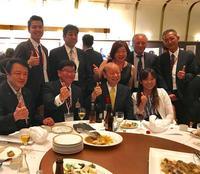 交流会の豪華な食事が配膳された円卓で親指を立てた市長と関係者8人が集合した写真
