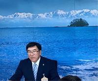 島が見える海の写真がある会見場で市長の胸から上が写っている写真