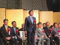東京富山県人会連合会の懇親の集いで金屏風の前で紹介されている市長の写真