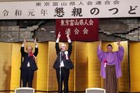 懇親のつどいのステージ上の金屏風前で朝乃山関と関係者2名がバンザイをしている写真
