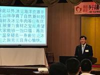 パーティー会場のステージ前に設置された中国語の文章が映し出されたスクリーンの横に立つ市長の写真