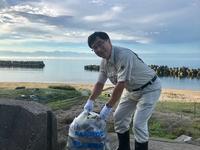 海岸で手袋をしてゴミが詰まった袋を持った市長の写真