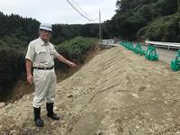 薮田見田窪線道路の脇が崩れた部分に土が盛られ緑のガードが設置された部分を指差す市長の写真