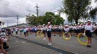 交通封鎖されている道路上で並んでアトラクションをする小学生の金管・鼓笛隊の写真