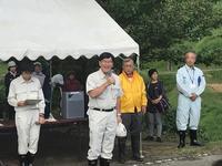 稲刈りのテント前に立ち作業服姿の市長がマイクで話している写真