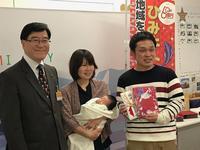 出生祝いののし袋と品を持つ男性と赤ちゃんを抱く女性と贈呈式で訪れた市長が並ぶ記念の写真
