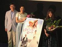 映画「ばぁちゃんロード」のパネルを持った女性と花束を持った女性の隣に市長が立っている写真