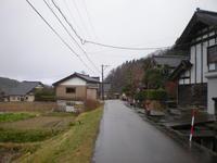 両端に家屋と草が生い茂っている所は走る舗装前の道路の写真