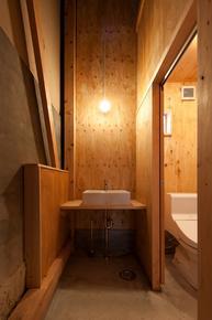 木の壁で仕切られたライト付きの手洗と新しい様式のトイレの写真