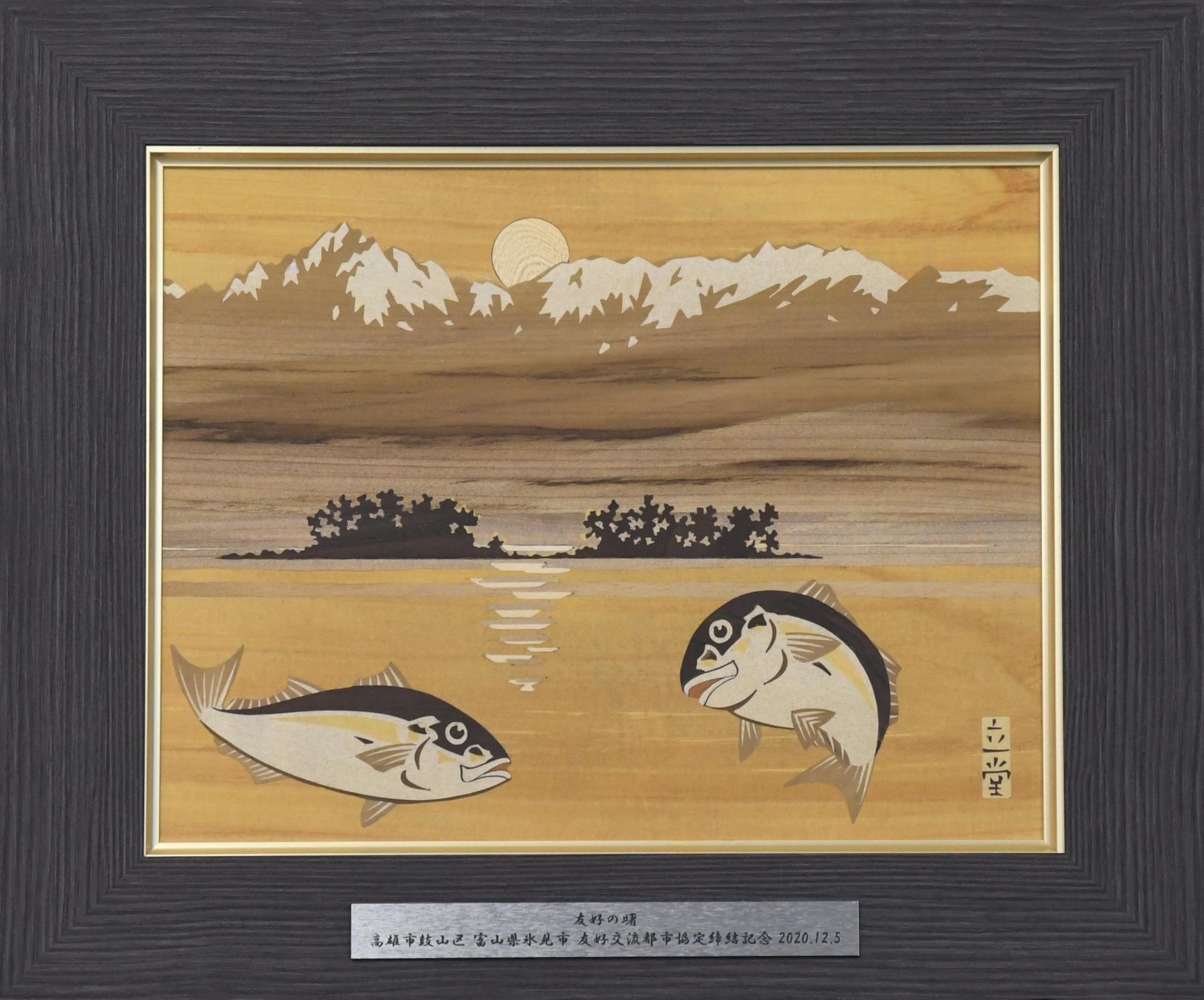 氷見市から寄贈した富山木象嵌の額装（2匹のブリが泳ぐ富山湾越しの立山連峰が描かれている）