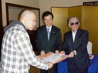 スーツを着た藤子先生と市長がもった賞状を受け取るチェックのシャツ姿の受賞者の男性の写真