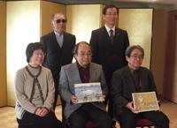 受賞作品を持って座っている受賞されたご夫婦の2名と男性1名が前列に並び藤子先生と市長が後列に並んだ集合写真