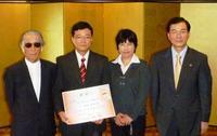 賞状を持つ大賞の男性と奥様をはさんで藤子先生と市長が並んだ集合写真