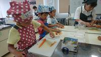 エプロンをした子どもたちがまな板で料理の材料を切っている写真