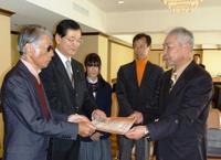 スーツ姿の藤子先生と市長がもった賞状を受け取る大賞の男性とそれを見つめる優秀賞の女子学生と男性の写真